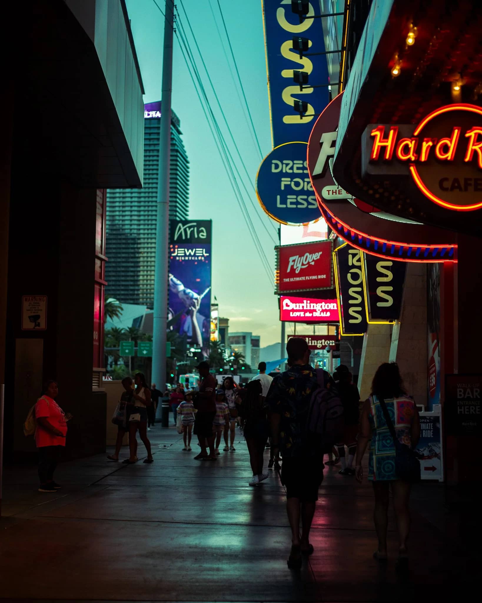 The Las Vegas Strip at dusk — the Hard Rock Cafe sign above a crowded sidewalk, layered neon and billboards receding down the street.